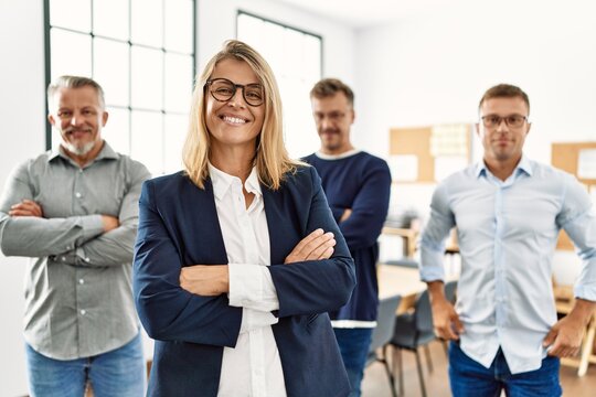 Middle age businesswoman smiling with arms crossed gesture standing with work partners at the office.