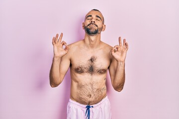 Young hispanic man shirtless wearing swimsuit relax and smiling with eyes closed doing meditation gesture with fingers. yoga concept.