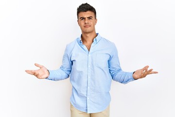 Young hispanic man wearing business shirt standing over isolated background clueless and confused...