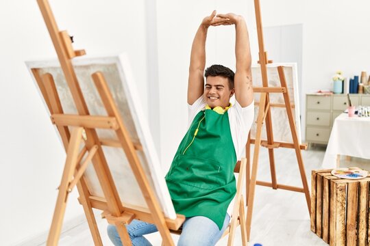 Young hispanic man smiling confident stretching arms at art studio