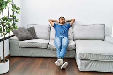 Young hispanic man relaxing sitting on the sofa wearing headphones at home