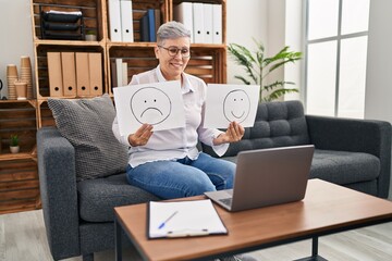 Middle age woman working on depression holding sad to happy emotion paper winking looking at the...