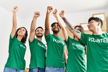 Fototapeta premium Group of young volunteers smiling happy with fists raised up at charity center.