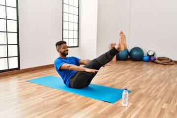 Fototapeta na wymiar Handsome hispanic man doing exercise and stretching on yoga mat, practicing flexibility and training at the gym