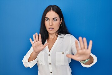 Young hispanic woman standing over blue background doing stop gesture with hands palms, angry and frustration expression