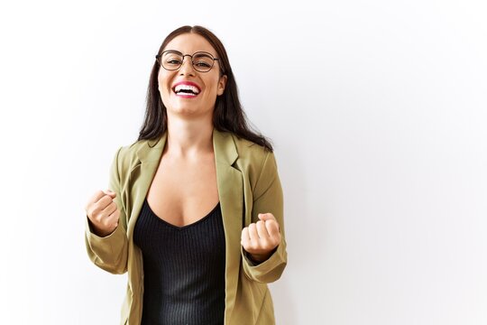 Young brunette woman standing over isolated background very happy and excited doing winner gesture with arms raised, smiling and screaming for success. celebration concept.