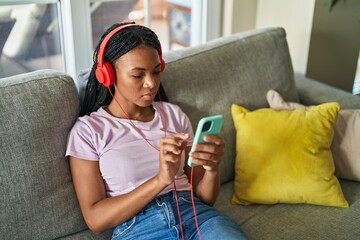 African american woman watching video on smartphone sitting on sofa at home