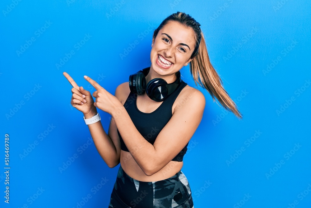 Poster beautiful hispanic woman wearing gym clothes and using headphones smiling and looking at the camera 