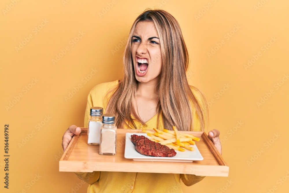 Poster beautiful hispanic woman holding tray with lunch angry and mad screaming frustrated and furious, sho