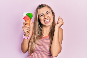 Beautiful hispanic woman holding ice cream screaming proud, celebrating victory and success very excited with raised arm