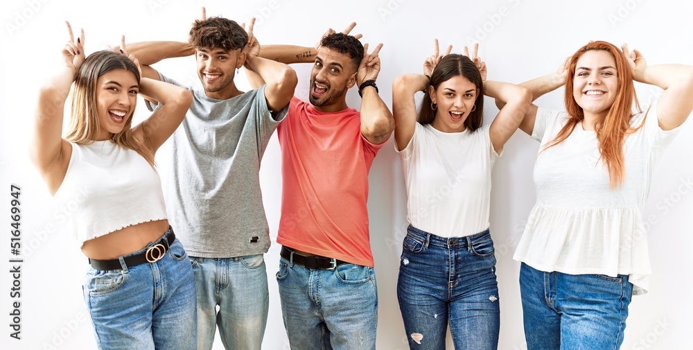 Sticker Group of young friends standing together over isolated background posing funny and crazy with fingers on head as bunny ears, smiling cheerful