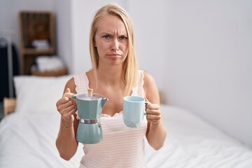 Young caucasian woman drinking coffee on the bed skeptic and nervous, frowning upset because of problem. negative person.