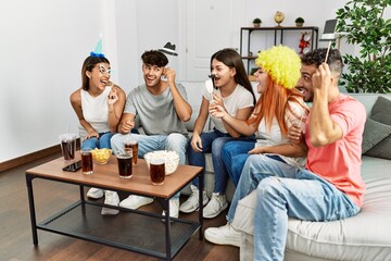 Group of young friends having party wearing funny costume accessories at home.