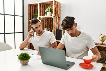 Two hispanic men couple talking on the smartphone and using laptop working at home
