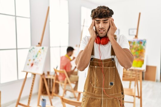 Young hispanic man at art studio with hand on head for pain in head because stress. suffering migraine.