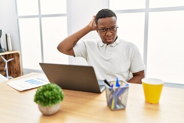 Young african man working at the office using computer laptop confuse and wondering about question....