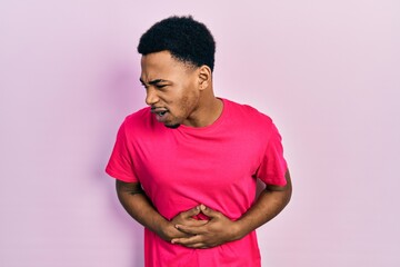 Young african american man wearing casua t shirt with hand on stomach because nausea, painful disease feeling unwell. ache concept.