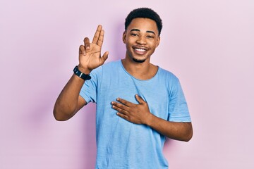 Young african american man wearing casual blue t shirt smiling swearing with hand on chest and...