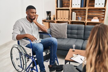 African american man doing therapy sitting on wheelchair looking stressed and nervous with hands on mouth biting nails. anxiety problem.