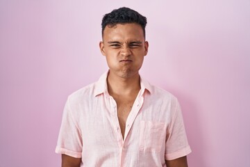 Young hispanic man standing over pink background puffing cheeks with funny face. mouth inflated...