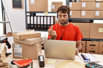 Young hispanic call center agent man working at warehouse showing middle finger, impolite and rude fuck off expression