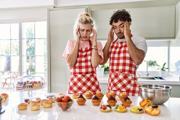 Couple of wife and husband cooking pastries at the kitchen with hand on head for pain in head because stress. suffering migraine.