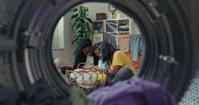 Happy loving helpful family finished cleaning clothes in the laundry room, they are sitting on the floor cuddling affectionately. Shot from inside the washing machine drum.