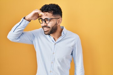 Hispanic man with beard standing over yellow background very happy and smiling looking far away...