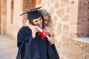 Two women mother and graduated daughter hugging each other at campus university