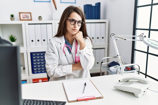 Young doctor woman wearing doctor uniform and stethoscope at the clinic with hand on chin thinking about question, pensive expression. smiling with thoughtful face. doubt concept.