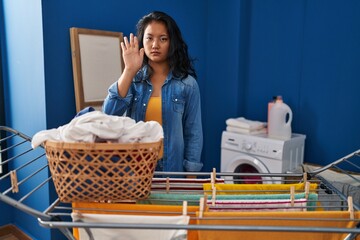 Young asian woman hanging clothes at clothesline doing stop sing with palm of the hand. warning expression with negative and serious gesture on the face.