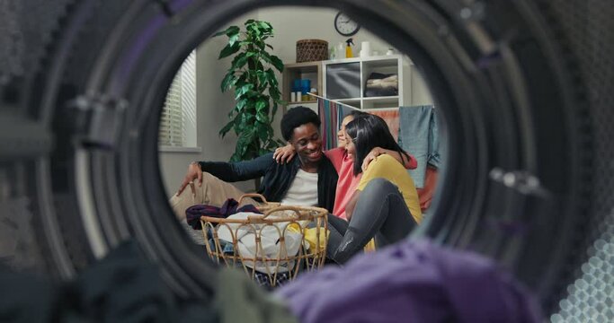 Happy loving helpful family finished cleaning clothes in the laundry room, they are sitting on the floor cuddling affectionately. Shot from inside the washing machine drum.
