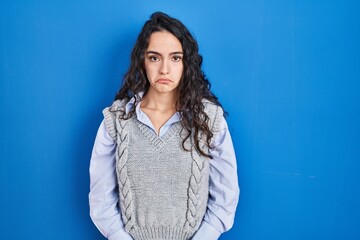 Young brunette woman standing over blue background depressed and worry for distress, crying angry and afraid. sad expression.
