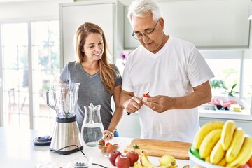 Middle age hispanic couple smiling happy cooking smoothie at the kitchen.