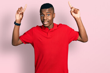 Young african american man wearing casual red t shirt smiling amazed and surprised and pointing up with fingers and raised arms.