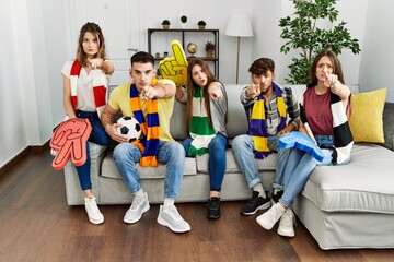 Group of young people watching football game wearing team scarf cheering game sitting on the sofa...