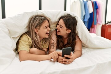 Young couple using smartphone covering with sheet lying on the bed.