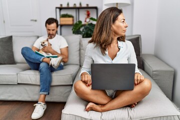 Hispanic middle age couple at home, woman using laptop looking to side, relax profile pose with natural face with confident smile.
