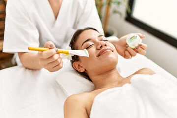 Obraz na płótnie Canvas Young latin woman relaxed having skin face aloe vera treatment at beauty center