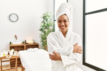 Young brunette woman wearing towel and bathrobe standing at beauty center happy face smiling with crossed arms looking at the camera. positive person.