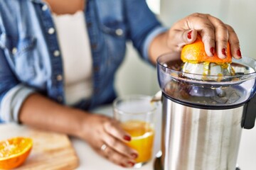 Hispanic brunette woman preparing orange juice at the kitchen