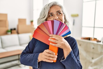 Middle age grey-haired woman covering face with color paint test at new home.