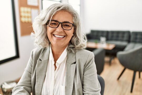 Middle age grey-haired businesswoman smiling happy working at the office.