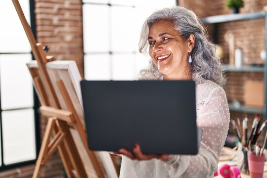 Middle age woman artist using laptop standing at art studio