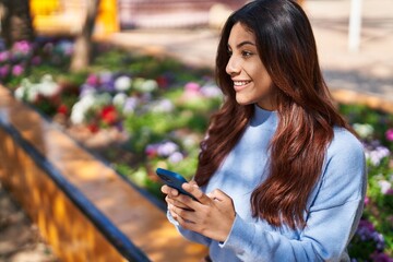 Young hispanic woman smiling confident using smartphone at park