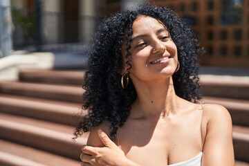 Young hispanic woman looking to the side touching arm at street