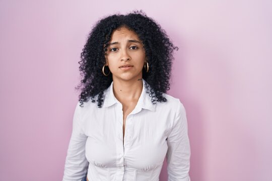 Hispanic woman with curly hair standing over pink background looking sleepy and tired, exhausted for fatigue and hangover, lazy eyes in the morning.