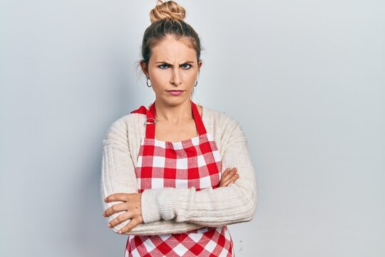 Beautiful caucasian woman with blond hair wearing apron skeptic and nervous, disapproving expression on face with crossed arms. negative person.