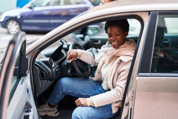 Fototapeta na wymiar African american woman smiling confident sitting on car at street