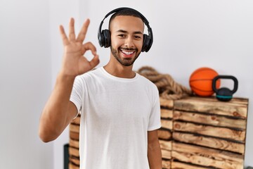 African american man listening to music using headphones at the gym smiling positive doing ok sign...